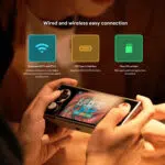 Primo piano delle mani che tengono AYANEO Pocket Micro e che visualizzano il gioco "Balatro" sullo schermo. In alto, le icone rappresentano le funzioni di connettività: WiFi 5 e BT 5.2 a doppia banda, interfaccia USB Type-C e slot per schede Micro SD, con brevi descrizioni dei vantaggi di ciascuna funzione.