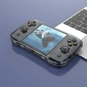 A transparent black gaming handheld device placed on a desk next to a laptop, displaying a futuristic spaceship on its screen.