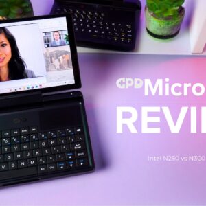 A dynamic thumbnail for a GPD MicroPC 2 review video. A black GPD MicroPC 2 is prominently featured in the foreground, open and angled towards the viewer, with its screen displaying a video conference call featuring a woman's face. The laptop's compact keyboard and trackpad are visible. The background is a white shelf with potted plants and another GPD MicroPC 2. The desk below the laptop is a vibrant pink and purple gradient. Large white text to the right of the laptop reads "GPD MicroPC 2 REVIEW", and smaller text below that says "Intel N250 vs N300" alongside the "Intel inside" logo.