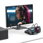 Namizna nastavitev, na kateri je računalnik GPD WIN 5 priklopljen in prek kablov povezan z zunanjim monitorjem. Ista slika ženskega lika z rožnatimi lasmi je prikazana na majhnem zaslonu konzole in velikem zunanjem monitorju, kar dokazuje zmožnost video izhoda doka. 