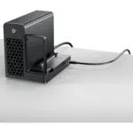 Boîtier NAS de bureau noir avec une baie de lecteur extractible et un évent hexagonal à l'avant, un bouton d'alimentation et un câble connecté sur une surface de bureau blanche.