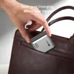 Hand placing a compact multi-port charger into a brown leather bag, promoting travel-friendly charging.